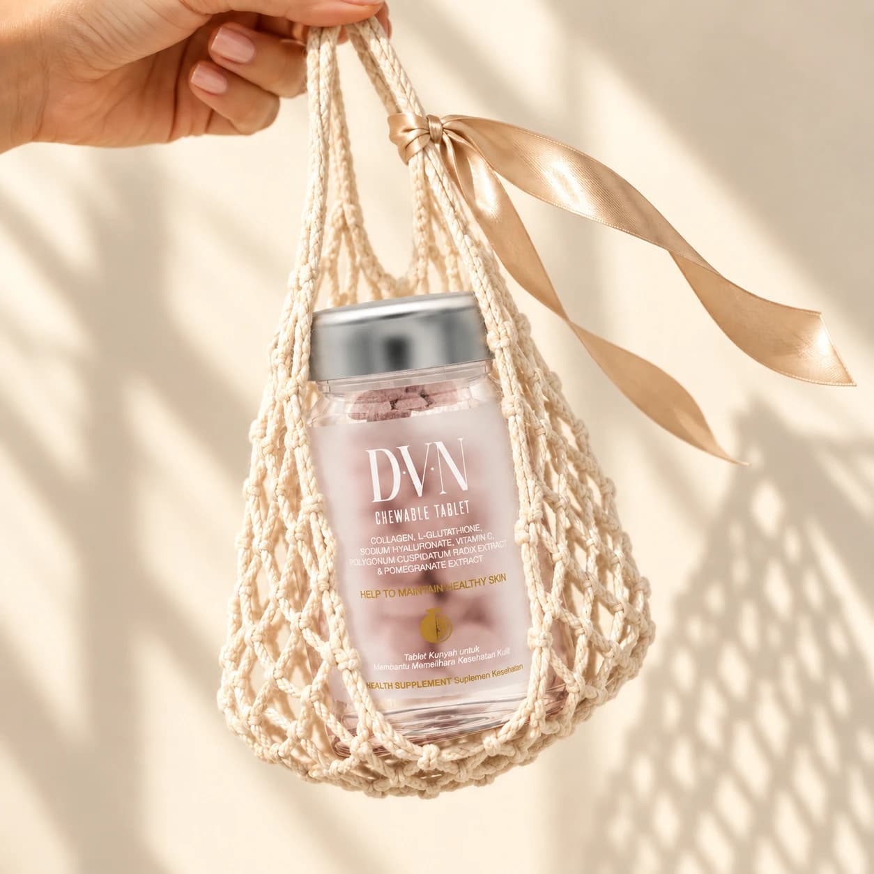 Botol DVN dalam tas jaring krem yang diangkat tangan dengan pita satin dan latar ivory