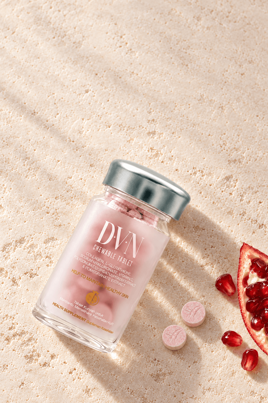 Botol DVN dan tablet pink di atas batu berwarna krem, dengan buah delima